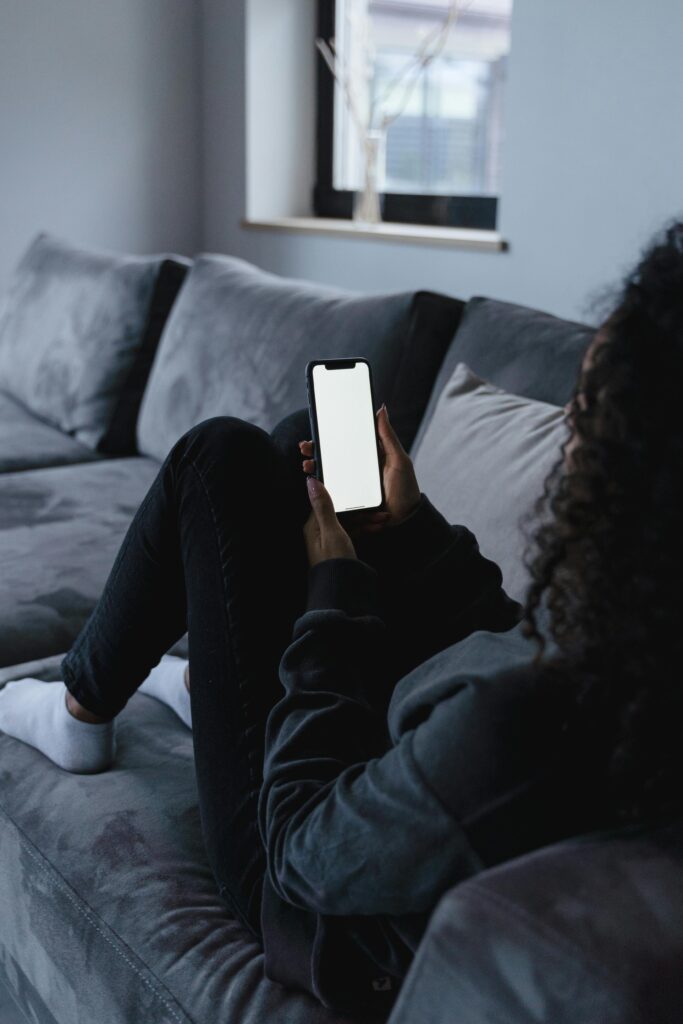 mulher utilizando celular em sofá para simbolizar uma pessoa realizando renda extra em casa